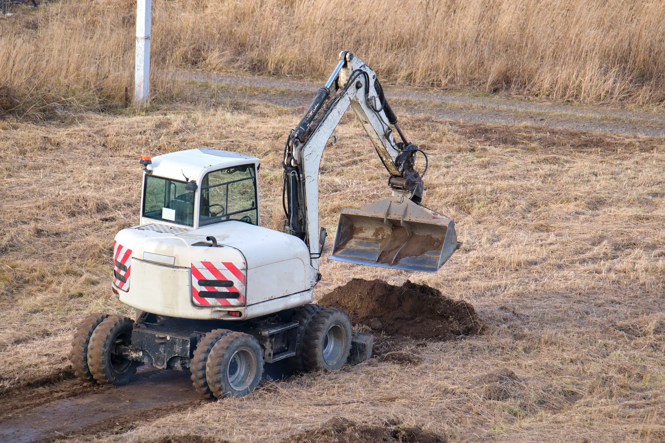 Minikoparka wykonująca wykop w ziemi na terenie działki, w otoczeniu trawy i łąk